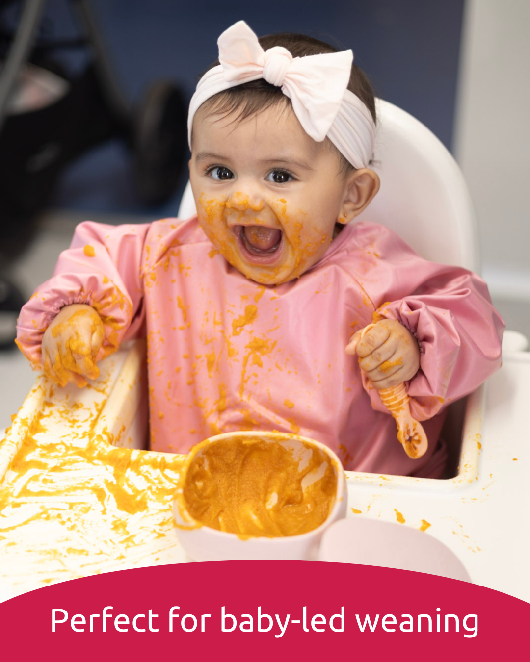 Baby getting messy in a pink baby smock.