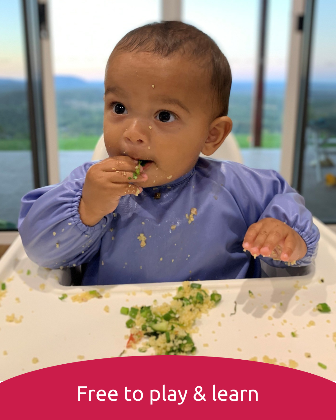 Baby feeding himself in a blue baby smock bib.