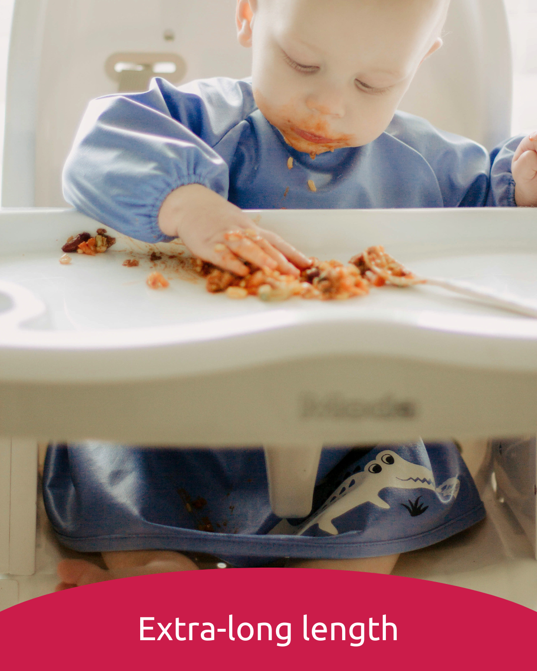 Baby wearing extra long blue feeding bib eating with his hands.