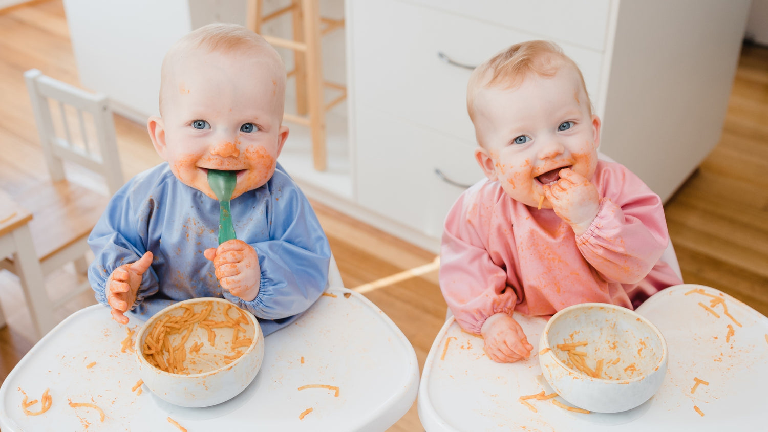Two babies wearing Smock Bibs in highchairs.