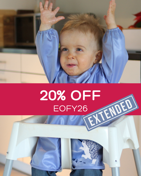 Toddler wearing a blue smock bib with his hands in the air.