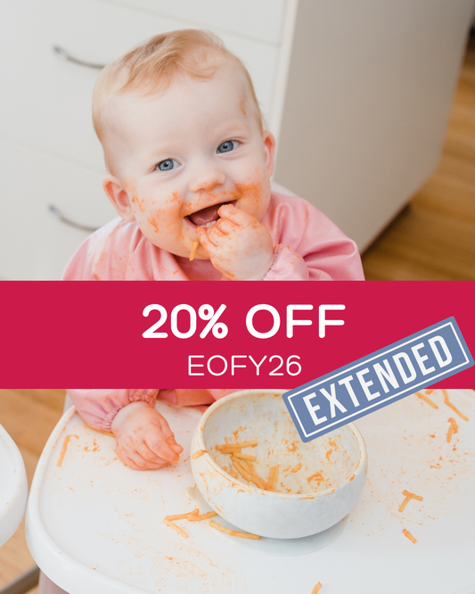 Baby wearing a pink baby smock bib feeding herself.
