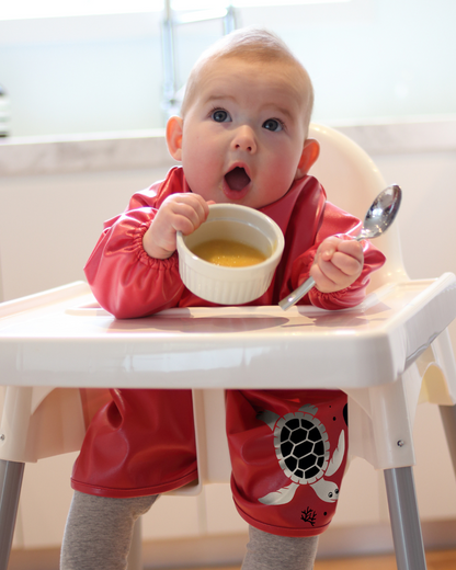 Baby wearing red extra long baby feeding smock.