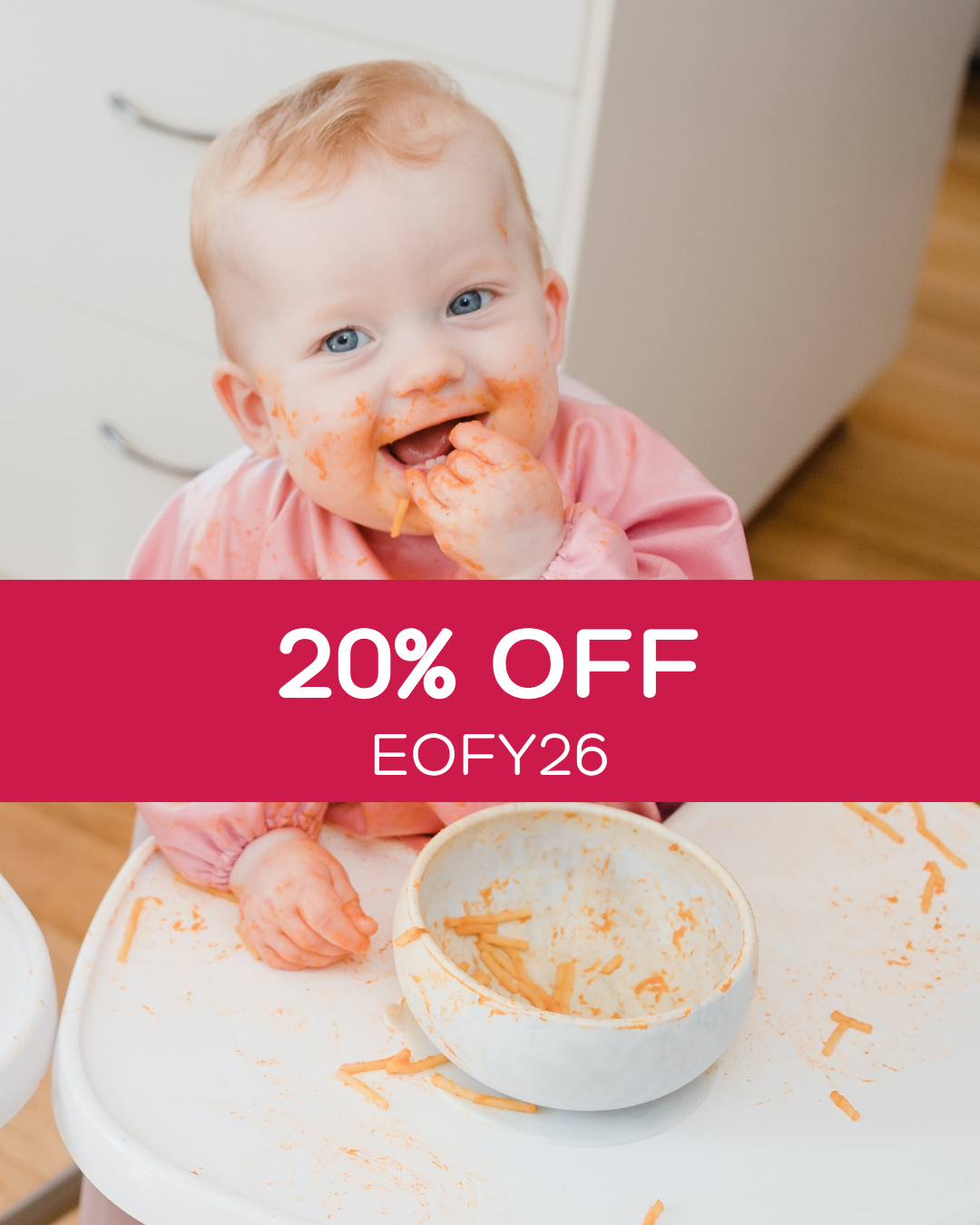 Baby wearing a pink baby smock bib feeding herself.