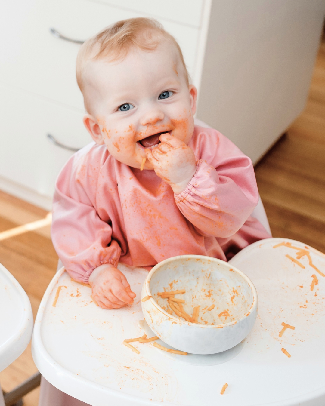 Baby wearing a pink baby smock bib feeding herself.