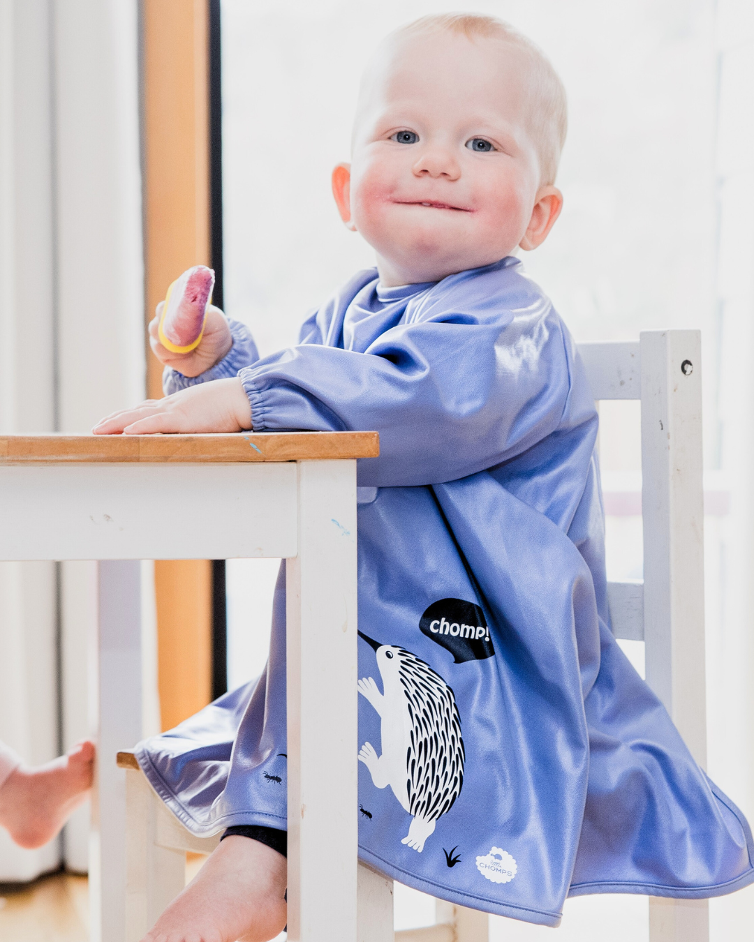 Child wearing a blue feeding smock with animal prints sitting at a table.