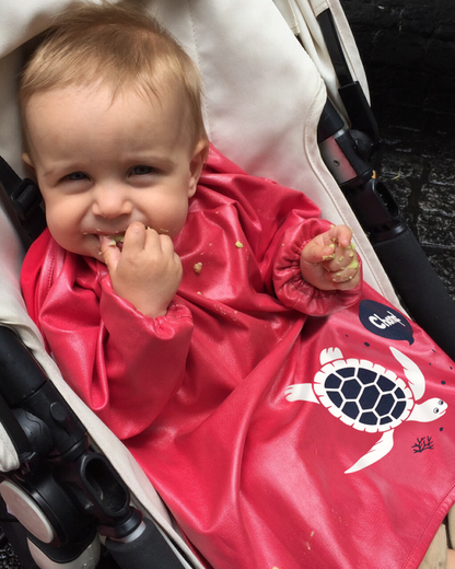 Baby wearing a red smock bib eating in a pram.