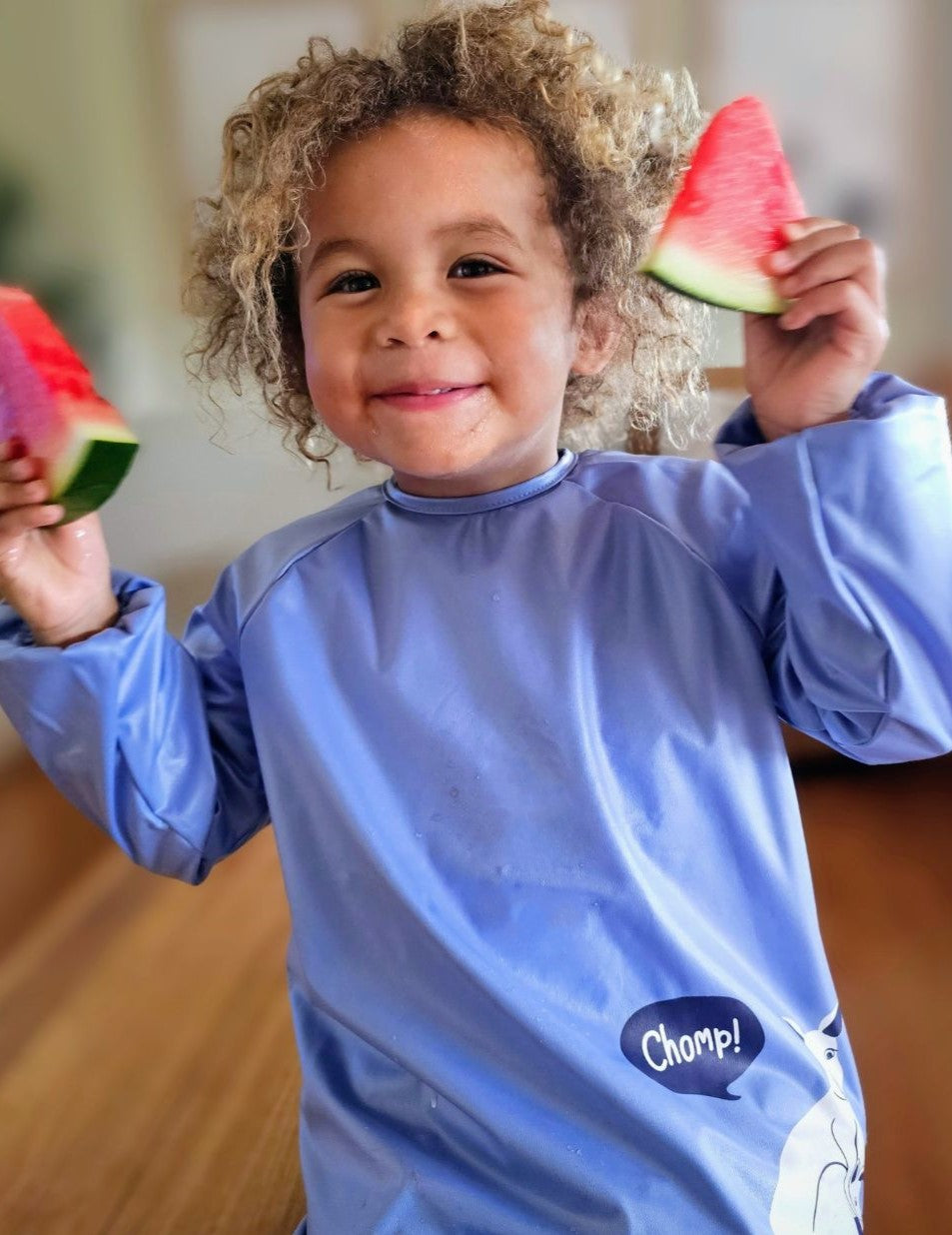 Boy wearing blue preschool smock bib eating watermelon.
