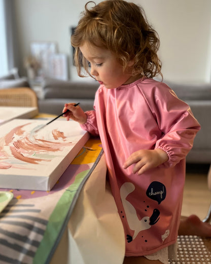 Toddler painting in pink child smock.