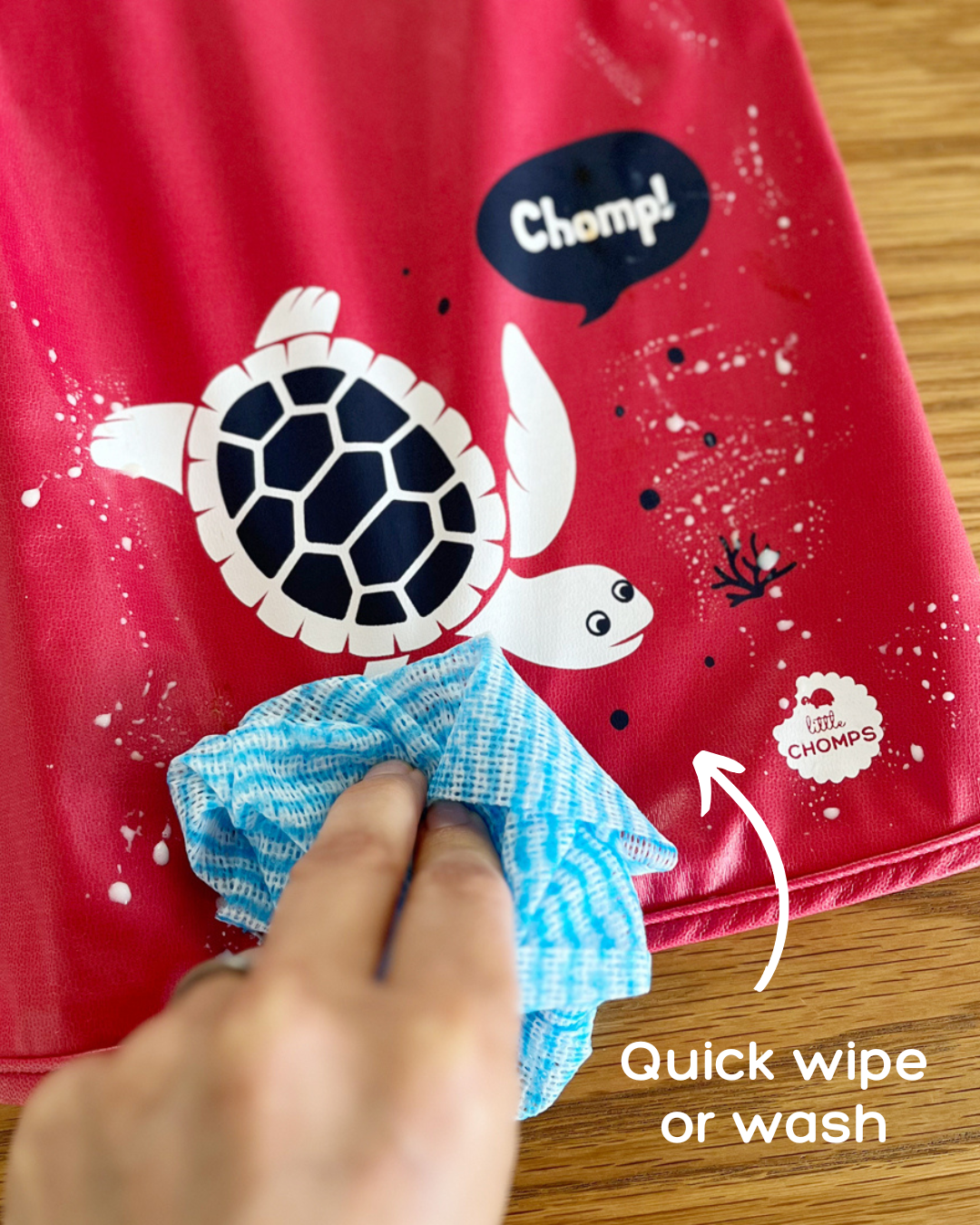 Hand wiping milk off a red baby apron.