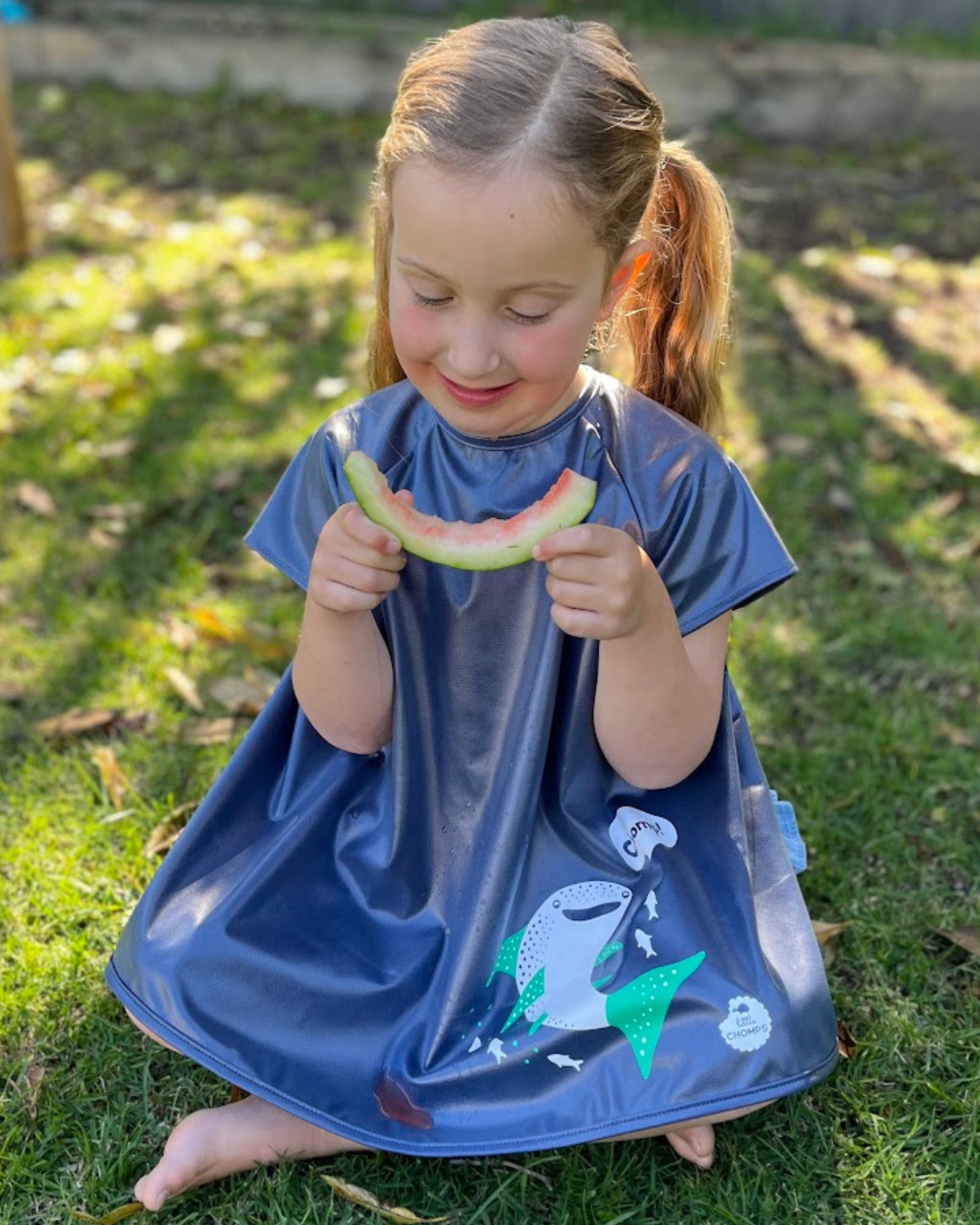 Girl wearing short sleeve smock bib eating watermelon.